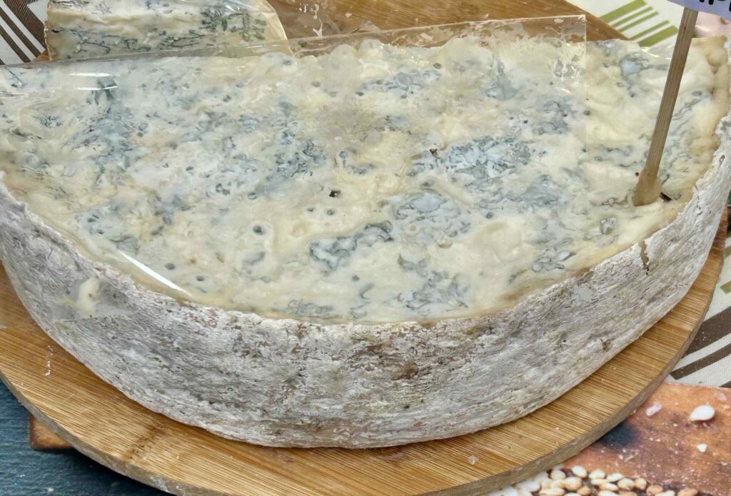 Forma di Gorgonzola DOP cremoso con venature blu su tagliere di legno.