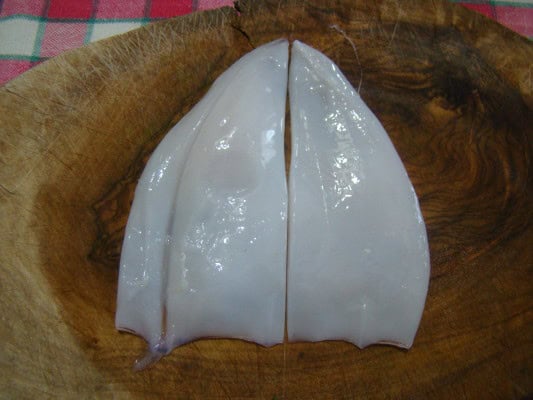 calamaro tagliato a metà per la preparazione degli spiedini di calamari alla romagnola, su tagliare di legno rustico