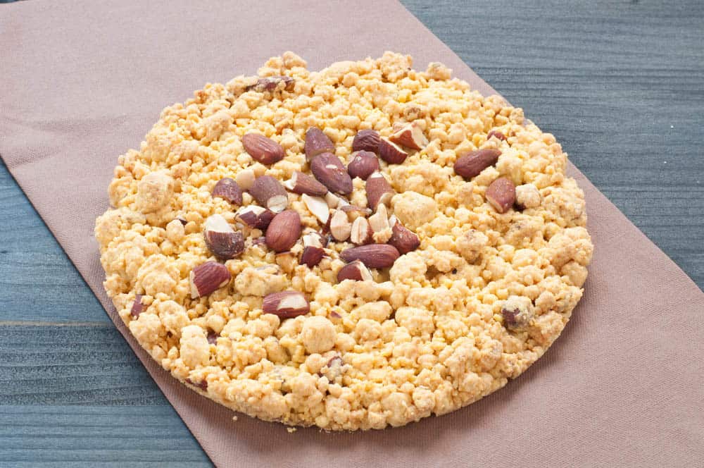 Torta sbrisolona mantovana con mandorle intere e superficie dorata servita su tagliere rustico