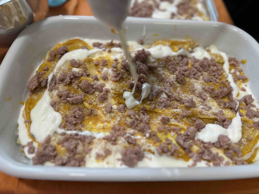Besciamella versata sulla lasagna con salsiccia e zucca.
