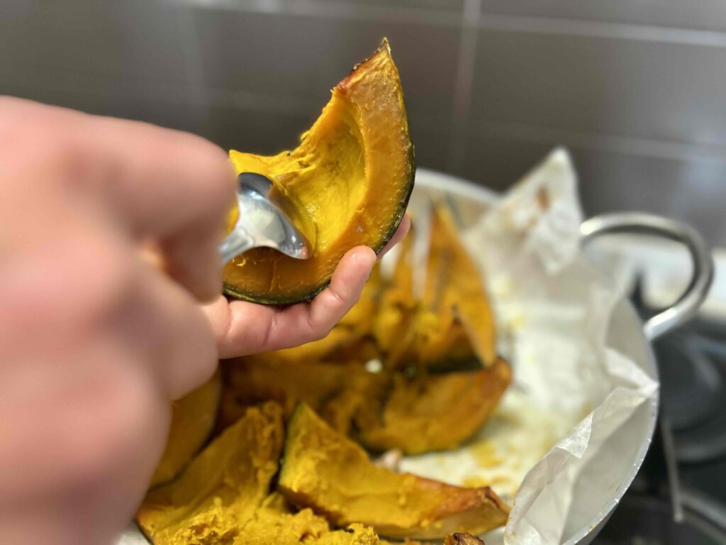 Mano che estrae la polpa dalla zucca cotta con un cucchiaio.