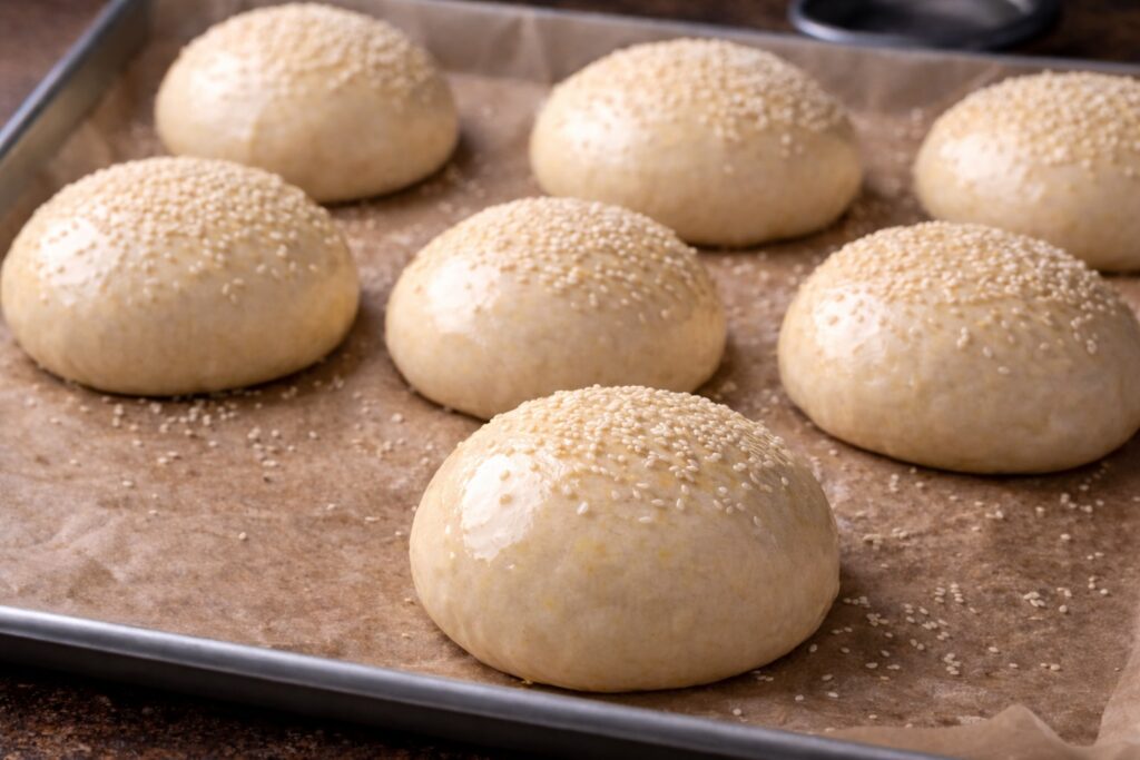 Panetti per bun da hamburger spennellati con uovo e cosparsi di sesamo prima della cottura